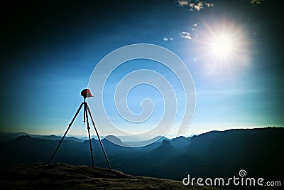 Tripod with red baseball cap on the peak ready for photography. Sharp autumn rocky peaks increased from heavy fog. Stock Photo
