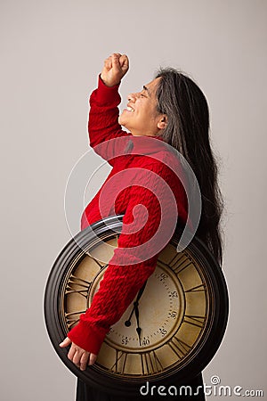 Triumphant Hispanic Woman Holding Clock Raises Fist Into The Air Stock Photo