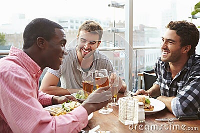 Trois amis masculins appréciant le déjeuner au restaurant de dessus de toit