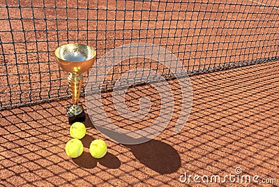 Trophy cup and tennis balls on a red clay court and shadow from the net. Champion trophy. Winner concept. Copy space Stock Photo