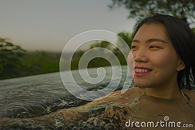 Tropical holidays lifestyle portrait of young beautiful and happy Asian Korean woman in bikini enjoying sunset at amazing jungle Stock Photo