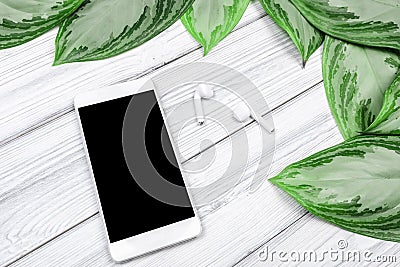 Tropical leaves and smartphone with earphones on white wooden background with text place Stock Photo