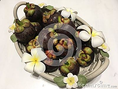 Tropical mangosteen fruits in ceramic basket, decorated with frangipani flowers Stock Photo