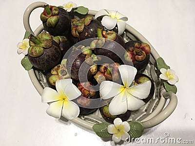 Tropical mangosteen fruits in ceramic basket, decorated with frangipani flowers Stock Photo