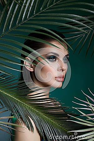 Tropical portrait sexy woman in leaves palm tree. Bright green makeup, shadow of palm leaves on girl face. Beautiful makeup Stock Photo