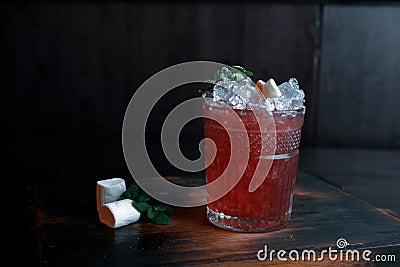 Tropical red alcoholic cocktail with the addition of: fresh juice, fruit syrup, mint, ice, fruit slices on a vintage wooden table Stock Photo