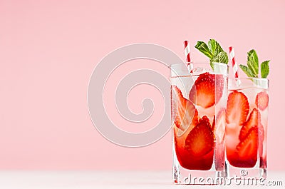 Tropical refreshing fruit drink with slices strawberry, green mint, ice, straw on soft light white wood board, pastel pink. Stock Photo