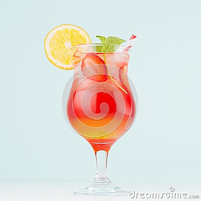 Tropical refreshing striped fruit drink sunrise with slices oranges, ice, strawberry, mint in wineglass on pastel green interior. Stock Photo