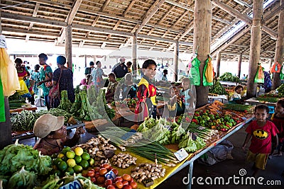 Tropical vegetables and fruits at market hall in Rabaul, Papua New Guinea. Young saleswoman wears shirt in national colors. Editorial Stock Photo