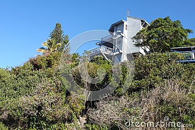 Tropical vegetation covers a hillside and almost hides steps up to a three story beach house on the top of the hill Stock Photo