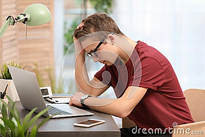 Troubled teenage boy with laptop at table Stock Photo
