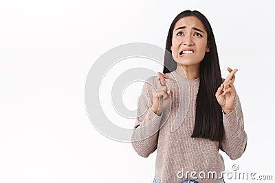 Troubled, worried cute asian girl in beige blouse, have concernes, cross fingers good luck, biting lip nervously look up Stock Photo