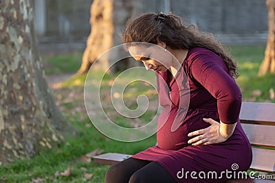 Troubled young pregnant woman on a park bench Stock Photo