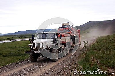 Truck carries all-terrain tracked vehicle at gravel road tundra Editorial Stock Photo