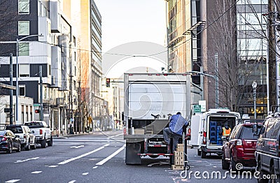 Truck driver of semi truck with box trailer unloading delivered cargo on the urban city street Editorial Stock Photo