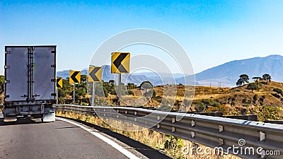 Truck driving on a road with dangerous curve signage Stock Photo