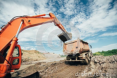 Trucks being loaded during highway construction site. Details of excavator scoop doing earthmoving works. Roadworks Stock Photo