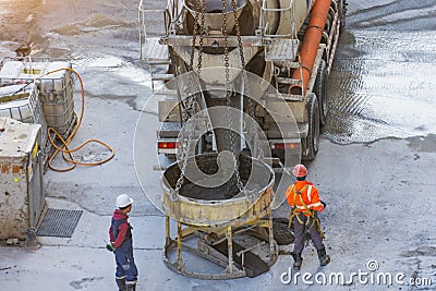 Trucks with a concrete mixer unloads concrete cement into a container suspended on the cables of a construction crane, workers Editorial Stock Photo