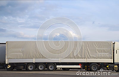 Trucks in the parking lot. In the foreground a truck with a long semi-trailer covered with a gray tarpaulin Stock Photo