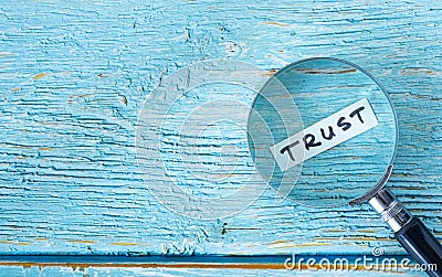 Trust handwritten word with a magnifying glass on blue wooden background Stock Photo