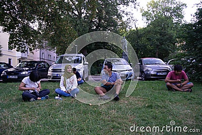 TUBINGEN/GERMANY-JULY 31 2018: A number of Asian tourists were sitting on the lawn, near the car park, talking to each other Editorial Stock Photo