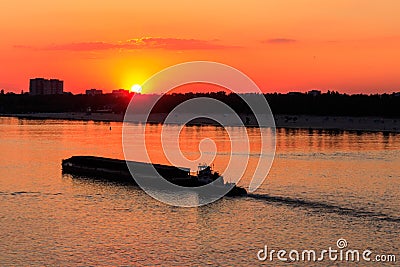 Tugboat pushing heavy long barge on the river Dnieper at sunset Stock Photo