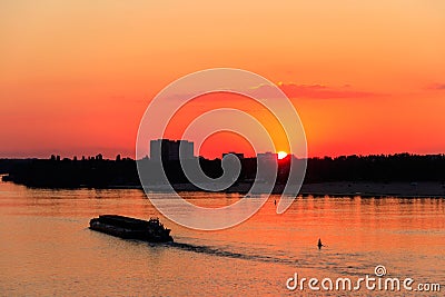 Tugboat pushing heavy long barge on the river Dnieper at sunset Stock Photo