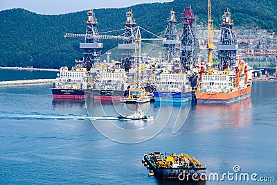 Tugboat sails pass driil ships in the Bay of Daewoo Shipbuilding and Marine Engineering DSME in Okpo city, South Korea. Editorial Stock Photo