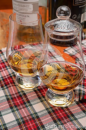 Tulip-shaped tasting glass with dram of Scotch single malt or blended whisky on wooden table with tartan Editorial Stock Photo