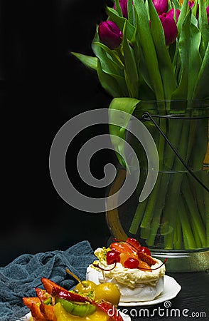 Tulip in vase with cup of coffee and fruit cake on dark background. Coffee time. Flower gift. Pavlova pie Stock Photo