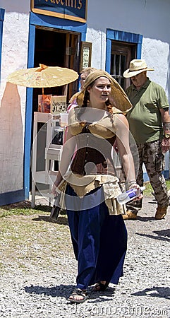 Costumed woman at Renaissance Faire with uncostumed couple walking behind her Editorial Stock Photo