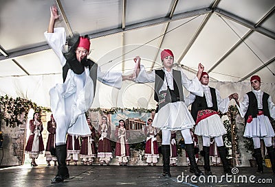 Costumed male Greek dancers in decorated tent venue featuring dramatic kick at Greek Festival in Tulsa Editorial Stock Photo