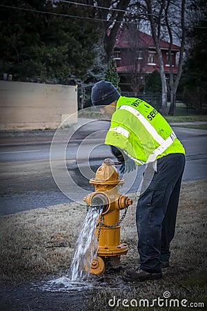 1-29-2019 Tulsa USA Waste and Sewer Worker turning off the water on a yellow fire hydrant near a wet street with two story house Editorial Stock Photo