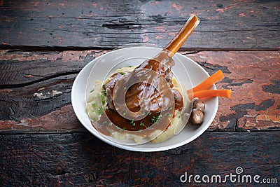 Turkish lamb shank in dark sauce with potato puree and vegetables on rustic wooden table Stock Photo