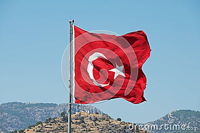Turkish National flag at the flagpole waves over a hill with a blue summer sky at the background in Bodrum, Turkey. Stock Photo