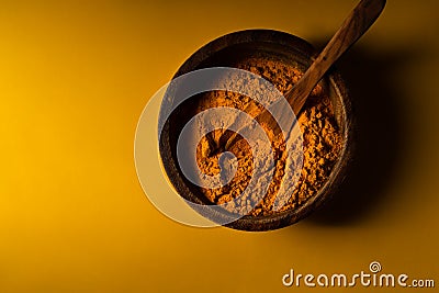 Turmeric powder in wooden bowl with wooden spoon on yellow background. Closeup view. Low key image with copy space Stock Photo