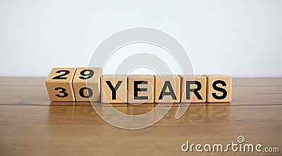 Turned cubes and changed the expression `29 years` to `30 years` or vice versa. Beautiful wooden table, white background. Busi Stock Photo