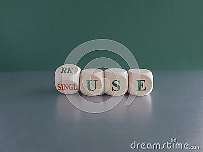 Turned a wooden cube and changes the green word single use to reuse. Beautiful green background, gray table. Stock Photo