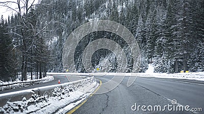 Turning winding divided highway road at winter dangerous condition with snow and ice and mountain with forest in Montana Stock Photo