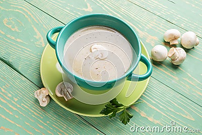 Turquoise ceramic bowl with mushroom cream soup on green plate on diagonal green wooden background Stock Photo