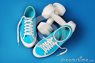 Turquoise gym shoes and white dumbbells on a blue sports mat Stock Photo