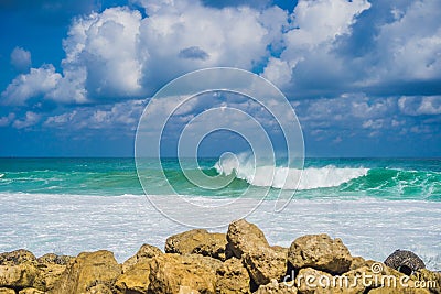 Turquoise rolling wave slamming on the rocks of the coastline Stock Photo