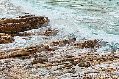 Turquoise rolling wave slamming on the rocks of the coastline Stock Photo