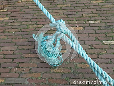 Turquoise rope with a knot above the pavement in the harbor Stock Photo