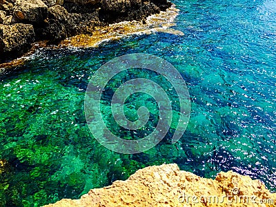 Turquoise sea water with grey natural stones. Purity ripple ocean water surface with selective focus and sun light. Transparent Stock Photo