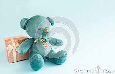 Turquoise soft teddy bear with an embroidered heart holds a gift box and a bow on a blue background. Children`s toy. Love, a gift Stock Photo