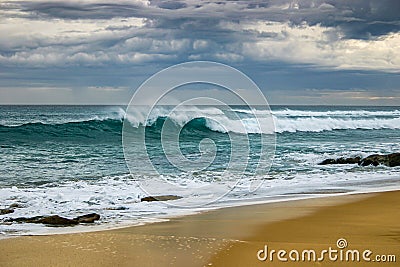 Turquoise wave crashing on beach set against an angry stormy sky Stock Photo