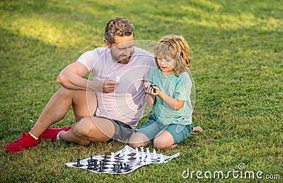 tutorship. daddy and child play logic game. father and son playing chess on grass in park. Stock Photo