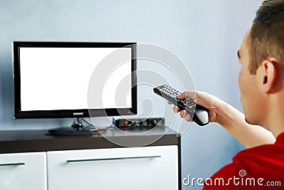 TV remote control in male hand in front of widescreen TV set with blank screen on blue wall background. Young guy switches channel Stock Photo