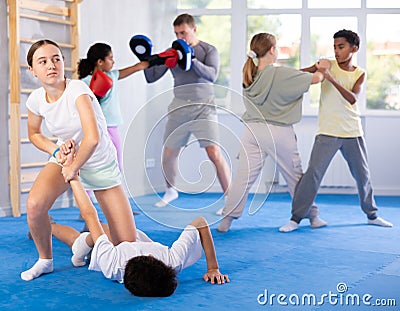 Tween girl applying armlock to face-down boy in mock fight at self-defense classes Stock Photo